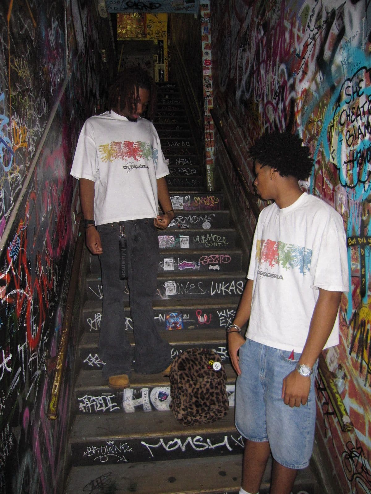 Two models in the multicolor eagle tee on a graffiti-covered stairwell