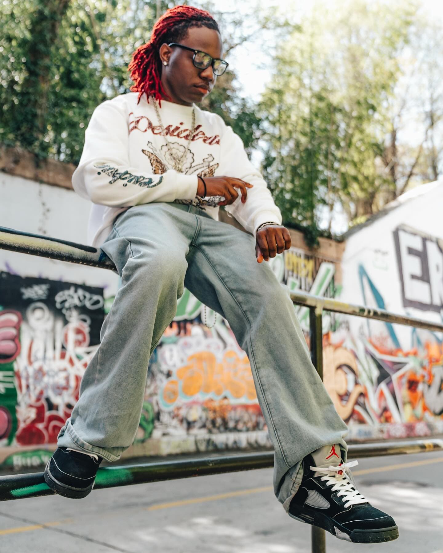 Perched on the rail, Jordans hanging over the graffiti wall
